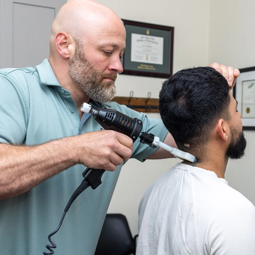Dr. Eric Chludzinski using an adjusting instrument on a patient’s neck